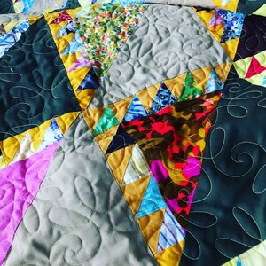 May include: A patchwork quilt with a variety of fabrics and colors, including green, yellow, pink, and blue. The quilt is made up of squares and triangles, and the fabric is sewn together in a random pattern. The quilt is quilted with a swirling pattern.