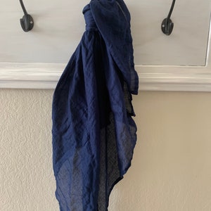May include: A dark blue cotton scarf hanging on a hook. The scarf is folded and draped over the hook.