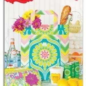 May include: A teal and yellow patterned folding tote bag with a green handle. The bag is filled with groceries, including a loaf of bread, a bottle of water, and a container of yogurt. The bag is sitting on a table with a floral patterned tablecloth.
