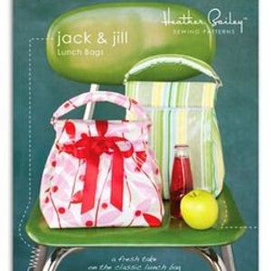 May include: Two lunch bags with handles, one pink with red accents and a bow, the other striped in green, white, and yellow. The bags are sitting on a green chair with a red apple and a glass bottle in front of them. The text "Jack & Jill Lunch Bags" is above the bags and "Heather Bailey Sewing Patterns" is above the text.