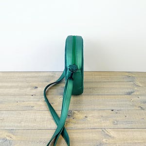 May include: A green round crossbody bag with a long adjustable strap. The bag has a zipper closure and a metal clasp.