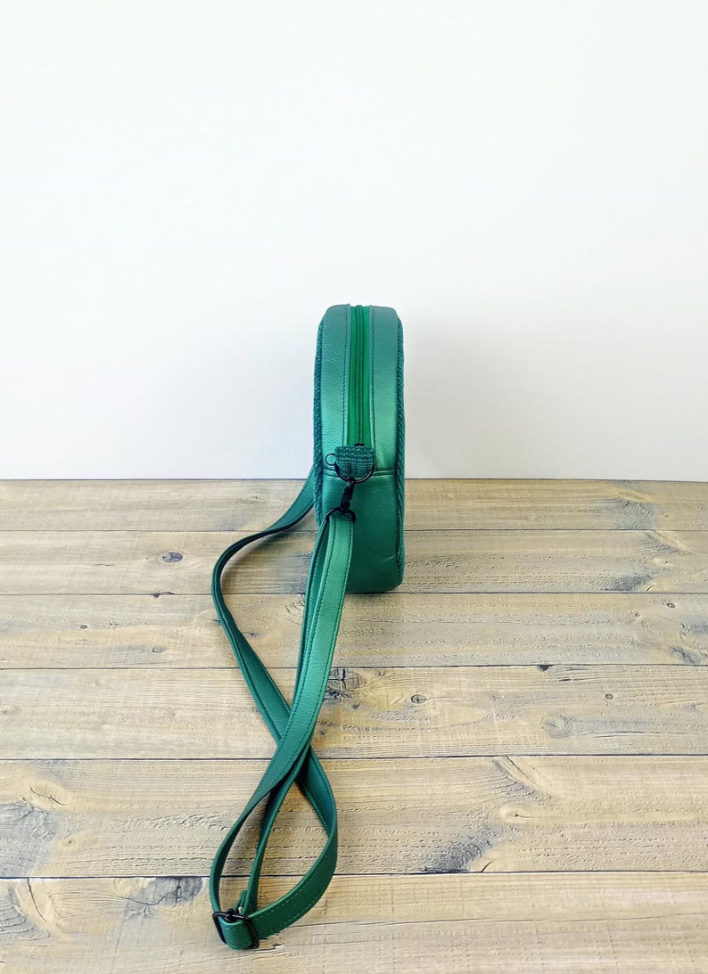 May include: A green round crossbody bag with a long adjustable strap. The bag has a zipper closure and a metal clasp.