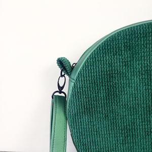 May include: A round green corduroy crossbody bag with a black strap and a silver clasp.