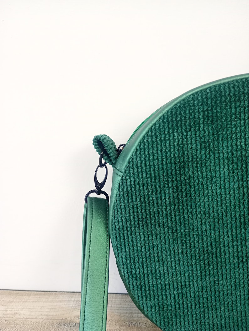 May include: A round green corduroy crossbody bag with a black strap and a silver clasp.
