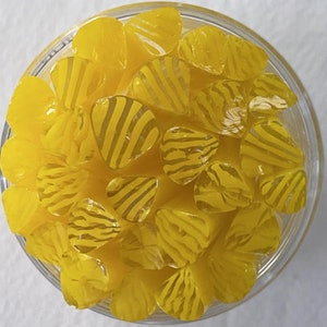 May include: A bowl filled with yellow and white striped glass pieces. The pieces are shaped like teardrops and have a glossy finish.