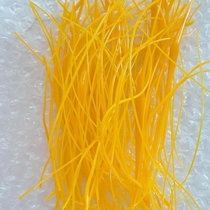 May include: A collection of numerous thin, flexible, bright yellow plastic strands arranged in a loose, tangled pile. Each individual strand is smooth, uniform in thickness, and semi-translucent, creating a vibrant and textured visual effect.