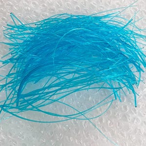 May include: A collection of numerous thin, flexible, translucent bright blue plastic filaments arranged in a loose, tangled pile. Each individual strand is smooth, cylindrical, and uniform in color, creating a vibrant, textured cluster.