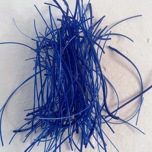 May include: A pile of thin, flexible, cobalt blue plastic rods. The rods are of varying lengths and are scattered across a white surface. The rods appear to be smooth and have a slight sheen, suggesting a glossy finish. The overall effect is a dense, tangled mass.