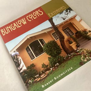 May include: A book titled "Bungalow Colors Exteriors" with a photo of a yellow house. The cover has a red and green color scheme with the title in gold lettering. The author's name, Robert Schweitzer, is at the bottom.