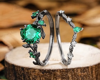 May include: A black and green engagement ring set with a large emerald green gemstone surrounded by smaller green gemstones and black metal leaves. The band is black and has a delicate design with small white gemstones.