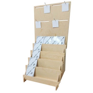 May include: A wooden display stand with five shelves for holding A6 size paper. The shelves are angled to create a tiered effect. The stand has a backboard with hooks for hanging items.