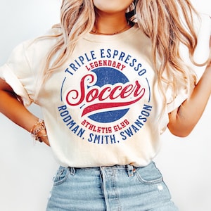 Puede incluir: Una camiseta blanca con un dise&ntilde;o gr&aacute;fico de estilo vintage con las palabras "Triple Espresso Legendary Soccer Rodman, Smith, Swanson Athletic Club".