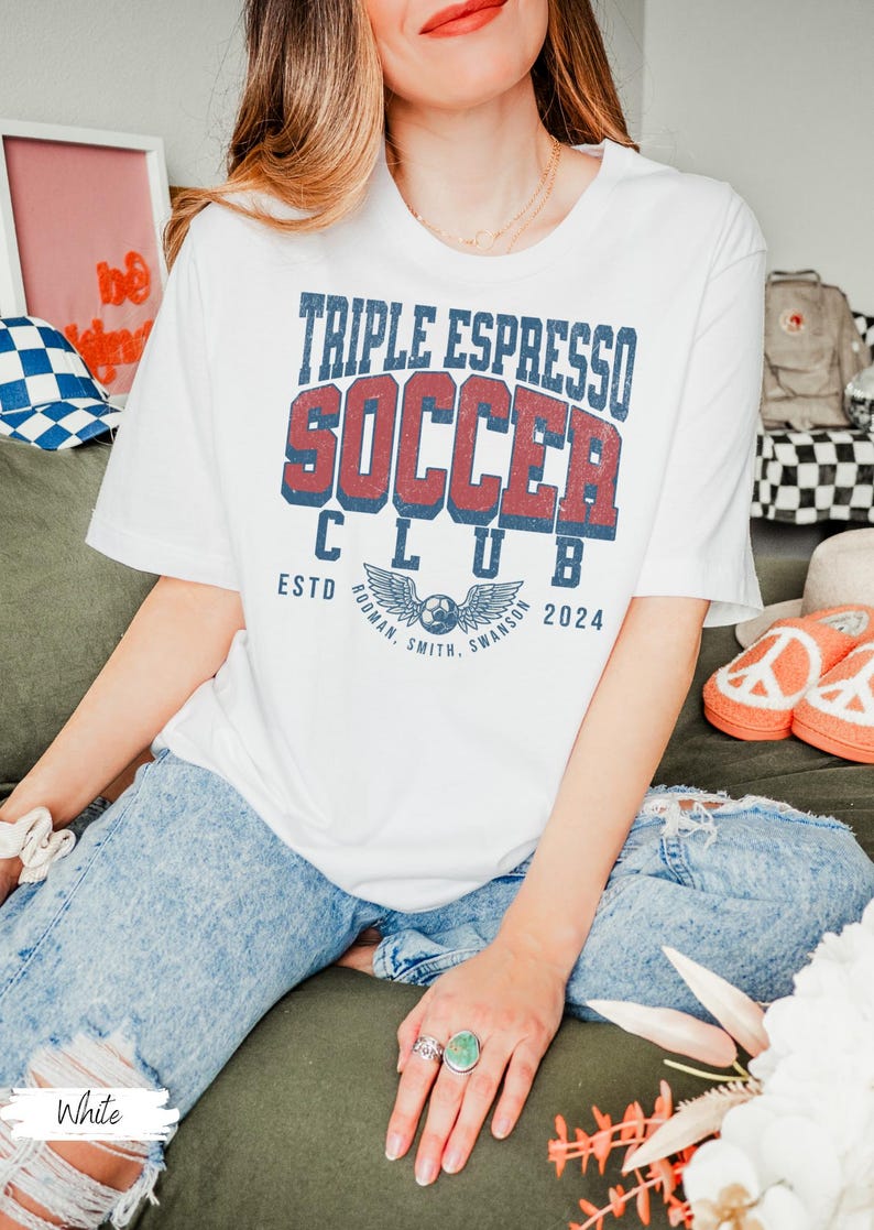 Op de afbeelding: Wit T-shirt met een vintage-stijl grafische afbeelding met de tekst "Triple Espresso Soccer Club" met een voetbal en vleugels. De tekst "Estd. 2024" staat onder de afbeelding.