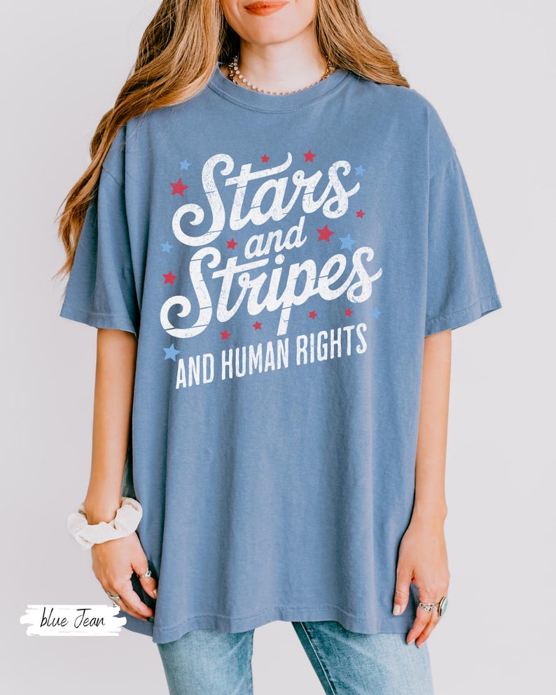 Puede incluir: Camiseta azul con el texto "Stars and Stripes AND HUMAN RIGHTS" en blanco, rojo y azul. La camiseta tiene un corte holgado y mangas cortas. El dise&ntilde;o incluye estrellas.