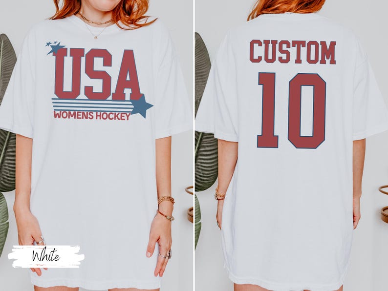 May include: White t-shirt with "USA WOMENS HOCKEY" in red and blue lettering. The back of the shirt features the word "CUSTOM" above the number "10" in red.