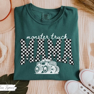 May include: A teal green t-shirt with the words "monster truck MAMA" in white. The word "MAMA" is in a black and white checkered pattern. A white monster truck graphic is below the text.