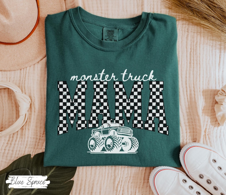 May include: A teal green t-shirt with the words "monster truck MAMA" in white. The word "MAMA" is in a black and white checkered pattern. A white monster truck graphic is below the text.