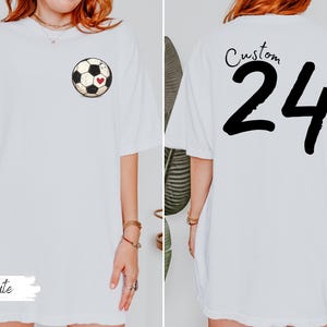 Op de afbeelding: Wit T-shirt met een voetbalafbeelding met een hart op de voorkant en het nummer 24 op de achterkant. Het woord "Custom" staat boven het nummer 24. Het woord "White" staat onderaan.