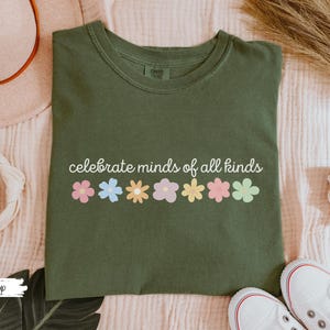 May include: A green t-shirt with the text "celebrate minds of all kinds" and a row of colorful flowers printed on the front.