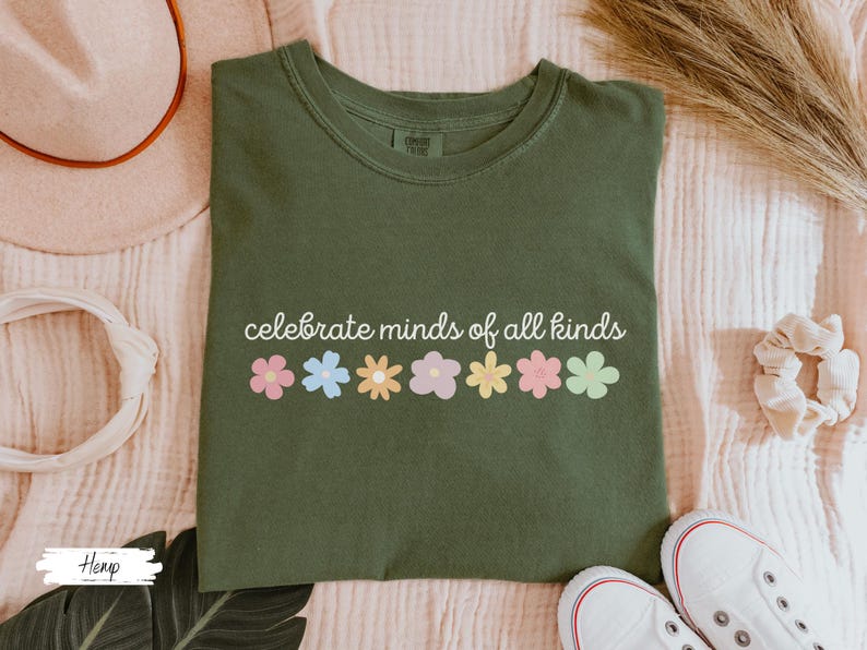 May include: A green t-shirt with the text "celebrate minds of all kinds" and a row of colorful flowers printed on the front.
