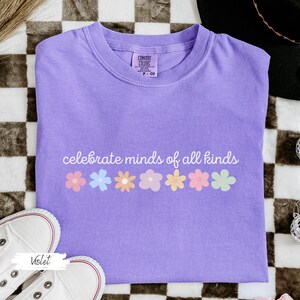 May include: A purple t-shirt with the text "celebrate minds of all kinds" and a row of colorful flowers printed on the front.