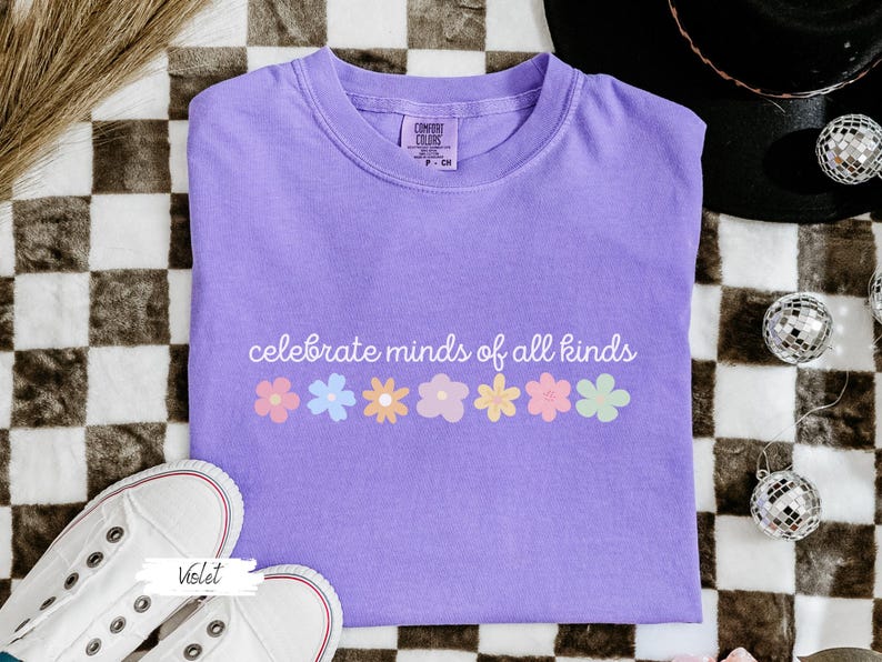 May include: A purple t-shirt with the text "celebrate minds of all kinds" and a row of colorful flowers printed on the front.