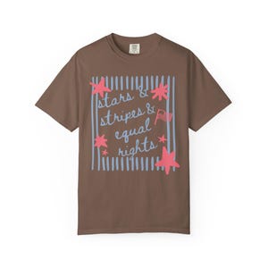 Puede incluir: Una camiseta marr&oacute;n con el texto "stars & stripes & equal rights" en un dise&ntilde;o azul y rosa. El dise&ntilde;o incluye estrellas, rayas y una peque&ntilde;a bandera americana. Una prenda informal para el d&iacute;a a d&iacute;a.