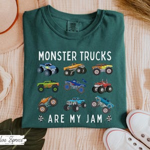 May include: Dark teal t-shirt with the text "MONSTER TRUCKS ARE MY JAM" and colourful monster truck graphics. The shirt features a crew neck and short sleeves. The shirt is made of a soft, comfortable material.