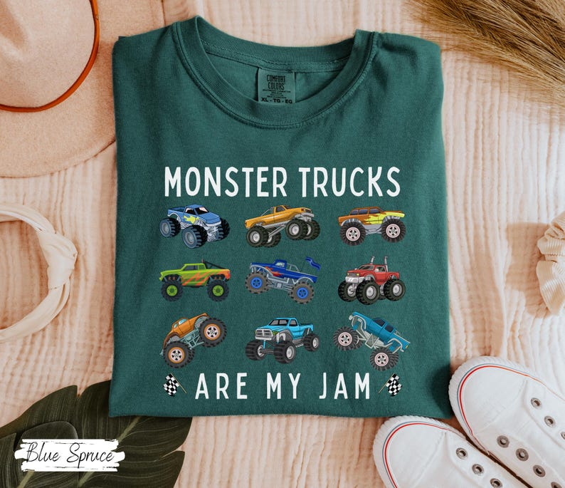May include: Dark teal t-shirt with the text "MONSTER TRUCKS ARE MY JAM" and colourful monster truck graphics. The shirt features a crew neck and short sleeves. The shirt is made of a soft, comfortable material.