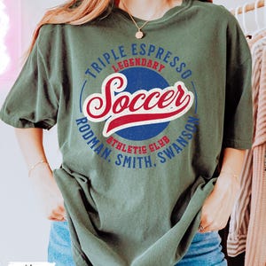 Puede incluir: Una camiseta verde con un dise&ntilde;o gr&aacute;fico de estilo vintage que incluye las palabras "Triple Espresso Legendary Soccer Rodman, Smith, Swanson Athletic Club".