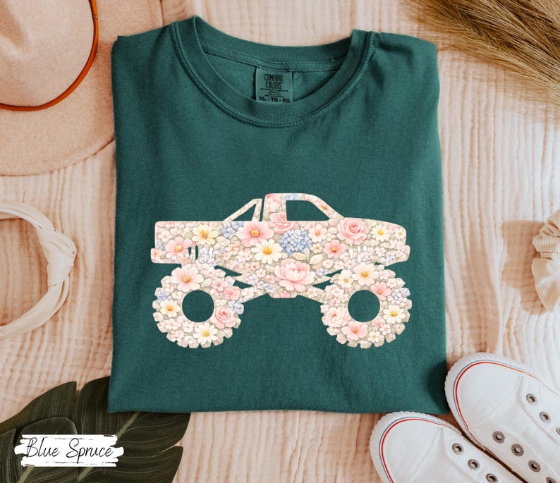 Op de afbeelding: Een donkergroen t-shirt met een bloemenmonster truck ontwerp. De truck is gevuld met roze, witte en gele bloemen. De tekst "Blue Spruce" staat linksonder.