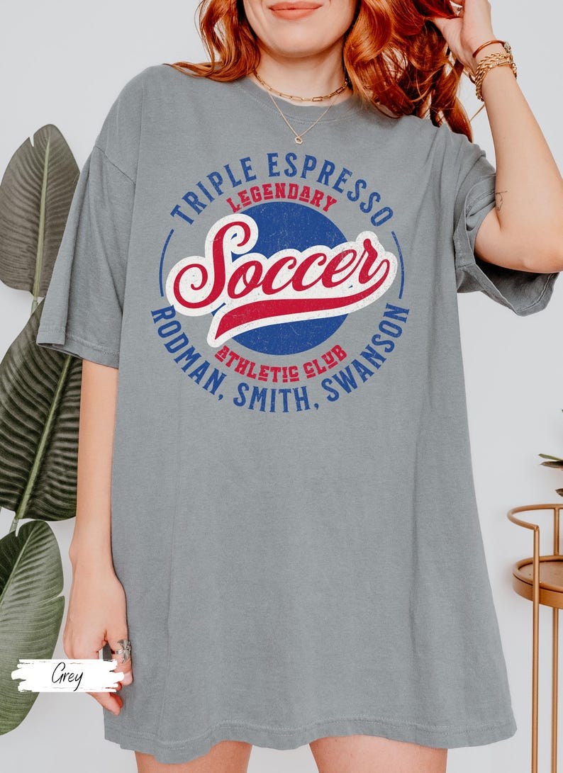 Puede incluir: Una camiseta gris con un dise&ntilde;o gr&aacute;fico de estilo vintage con las palabras "Triple Espresso Legendary Soccer Rodman, Smith, Swanson Athletic Club".
