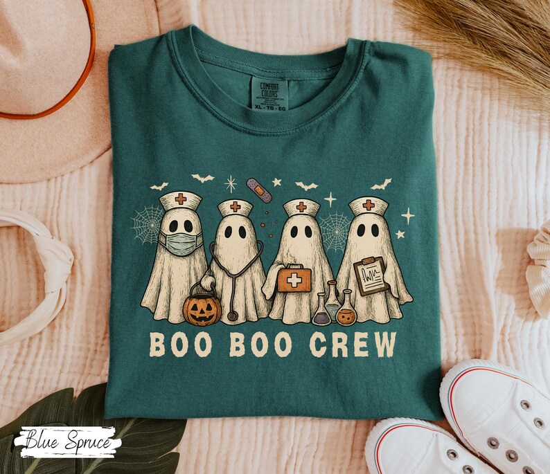 May include: Teal-colored t-shirt featuring a graphic of four ghost characters dressed as medical professionals. The ghosts are wearing medical hats, masks, and carrying medical tools. The text "BOO BOO CREW" is printed below the ghosts.