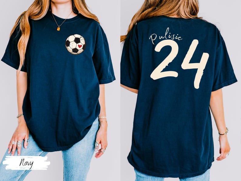 Op de afbeelding: Marineblauw T-shirt met een voetbalafbeelding en een rood hart op de voorkant. De achterkant van het shirt toont de naam "Pulisic" boven het nummer "24" in cr&egrave;me. Een casual, comfortabele stijl.