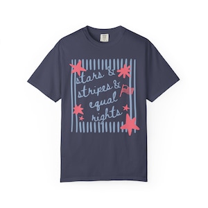 Puede incluir: Camiseta azul marino con el texto "stars & stripes & equal rights" en un dise&ntilde;o blanco y rojo. El dise&ntilde;o incluye estrellas rojas, rayas azules y una peque&ntilde;a bandera americana. La camiseta es de estilo casual y de manga corta.