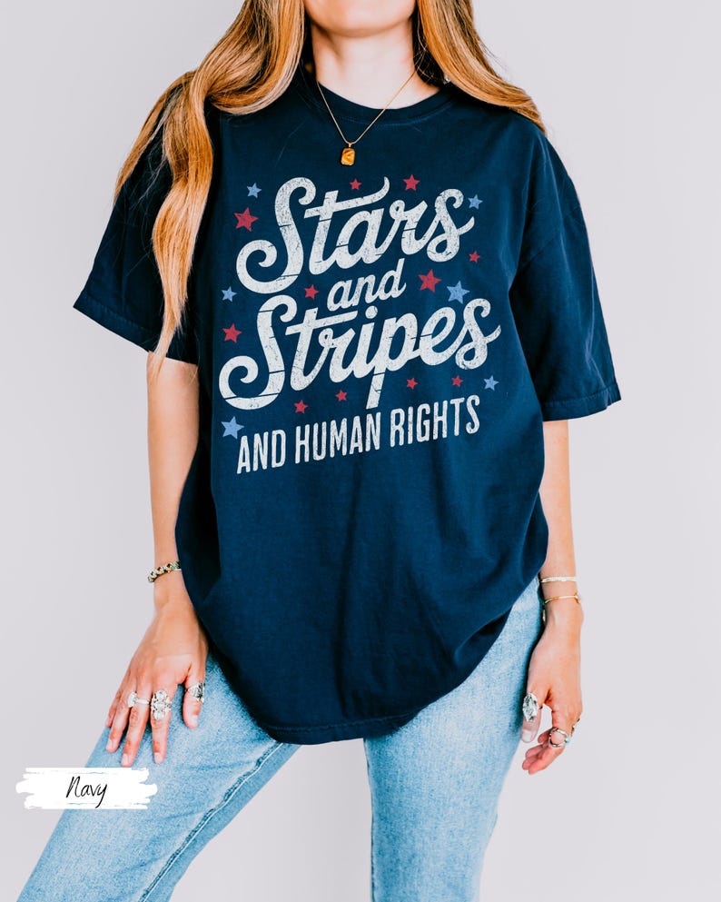 Puede incluir: Camiseta azul marino con el texto "Stars and Stripes AND HUMAN RIGHTS" en blanco, rojo y azul. El dise&ntilde;o incluye estrellas. La camiseta es una prenda informal de manga corta.