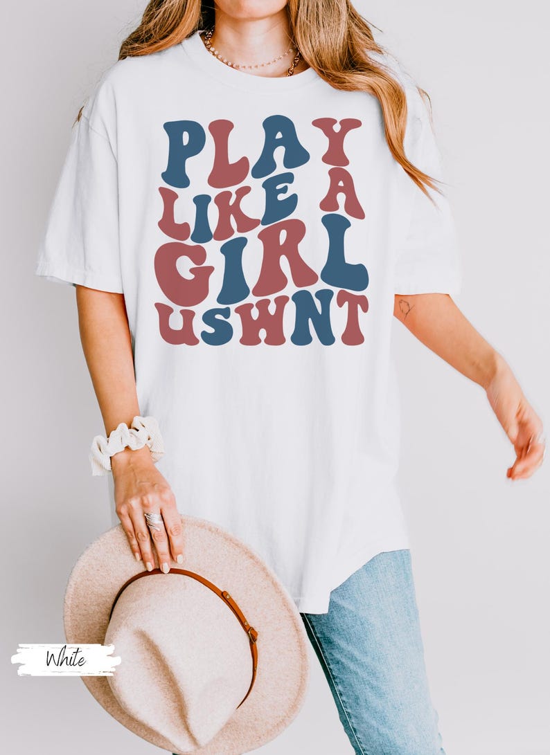 May include: White oversized t-shirt with the text "PLAY LIKE A GIRL USWNT" in blue and red retro font.