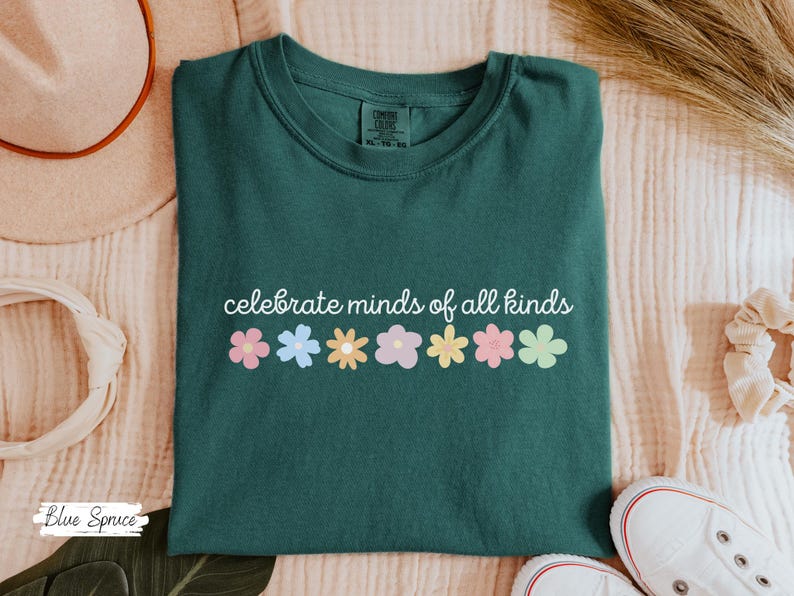 May include: A dark green t-shirt with the text 'celebrate minds of all kinds' in white. The text is surrounded by a row of colorful flowers.