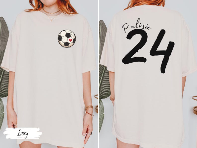 Op de afbeelding: Ivoor kleurig T-shirt met een voetbalafbeelding en een rood hart. De achterkant van het shirt toont de naam "Pulisic" boven het nummer "24" in zwart. Het shirt heeft een casual, oversized pasvorm.