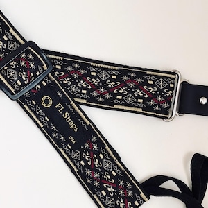 May include: Black guitar strap with a woven pattern featuring red, gold, and white geometric designs. The strap has black leather ends and metal hardware. The text "FL Straps USA" is visible on the strap.