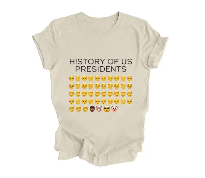 Pu&ograve; includere: Una maglietta beige con la scritta "HISTORY OF US PRESIDENTS" stampata sul davanti. Il testo &egrave; seguito da una griglia di faccine emoji gialle.
