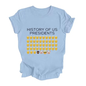 Pu&ograve; includere: Maglietta blu chiaro con il testo "HISTORY OF US PRESIDENTS" e una griglia di emoji gialli con facce sorridenti, tra cui alcune varianti.