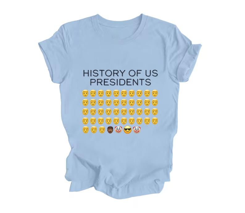 Pu&ograve; includere: Maglietta blu chiaro con il testo "HISTORY OF US PRESIDENTS" e una griglia di emoji gialli con facce sorridenti, tra cui alcune varianti.