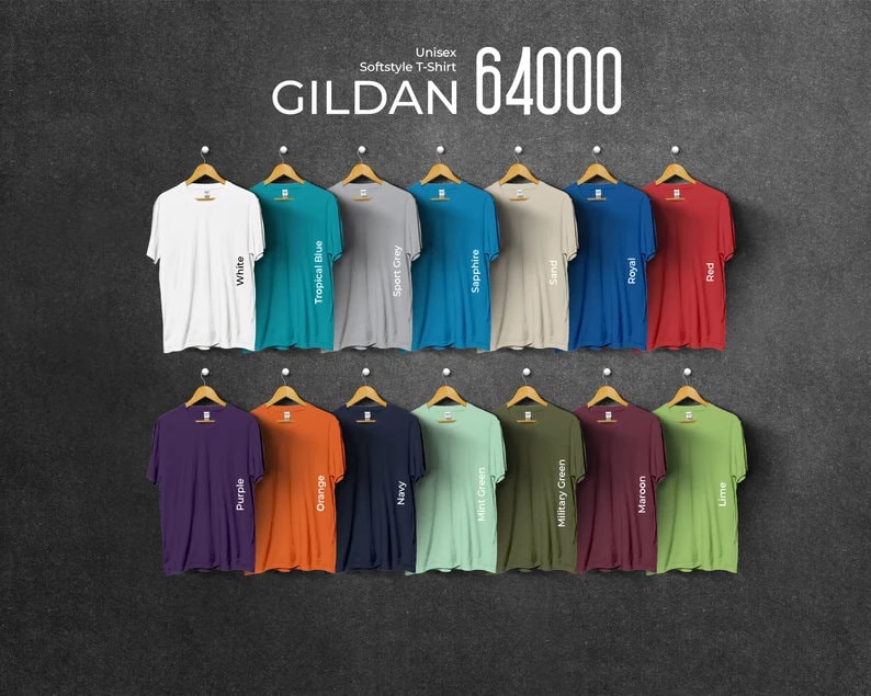 Pu&ograve; includere: Esposizione di magliette unisex Gildan 64000 Softstyle in vari colori, tra cui bianco, rosso e blu navy. Ogni maglietta &egrave; appesa a una gruccia di legno su uno sfondo grigio scuro. Il testo "GILDAN 64000" &egrave; visualizzato in alto.