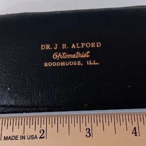 May include: Black leather eyeglasses case with gold lettering that reads "DR. J R. ALFORD Optometrist ROODHOUSE, ILL."
