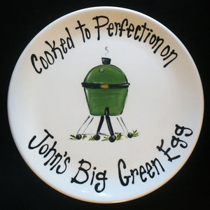 May include: White ceramic plate with a green and black illustration of a grill with the text "Cooked to Perfection on John's Big Green Egg".