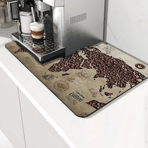 May include: A stainless steel espresso machine with a cup of coffee on the drip tray. A rectangular coffee-themed mat with a world map design made of coffee beans is in front of the machine.