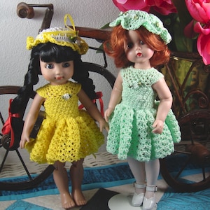 May include: Two dolls wearing crocheted dresses and hats. The doll on the left is wearing a yellow dress and a white hat with a red ribbon. The doll on the right is wearing a green dress and a white hat with green accents.