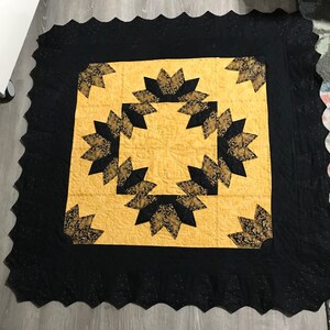 May include: A black and gold quilt with a scalloped edge. The quilt features a repeating pattern of eight-pointed stars.