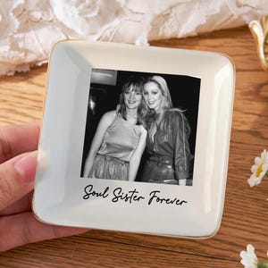 May include: Square, off-white ceramic trinket dish with a gold rim, featuring a black and white photo of two women. The words "Soul Sister Forever" are written below the photo in a script font.